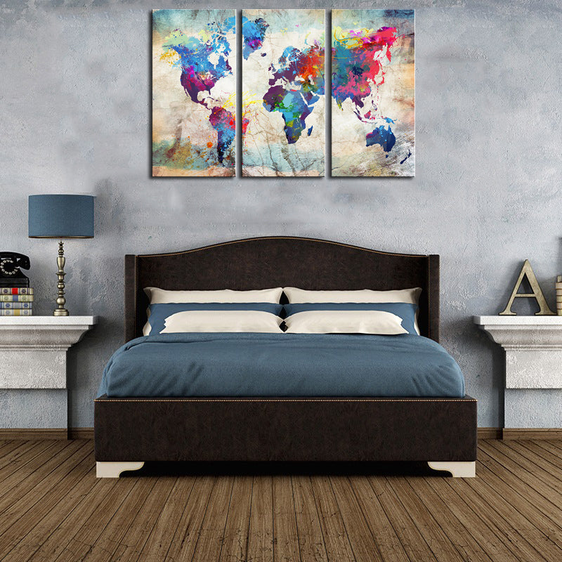 World Map in Paint Spatter - Vibrant colorful three-panel canvas art featuring world continents in watercolor splashes and paint splatters on a textured beige background, displayed above a bed in modern bedroom decor