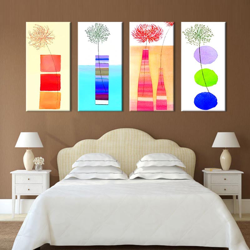 Modern Kitchen Panels featuring four vibrant canvas artworks displaying abstract floral designs in red, green, and pink, with geometric shapes in bright colors against cream backgrounds, arranged horizontally above a bed.