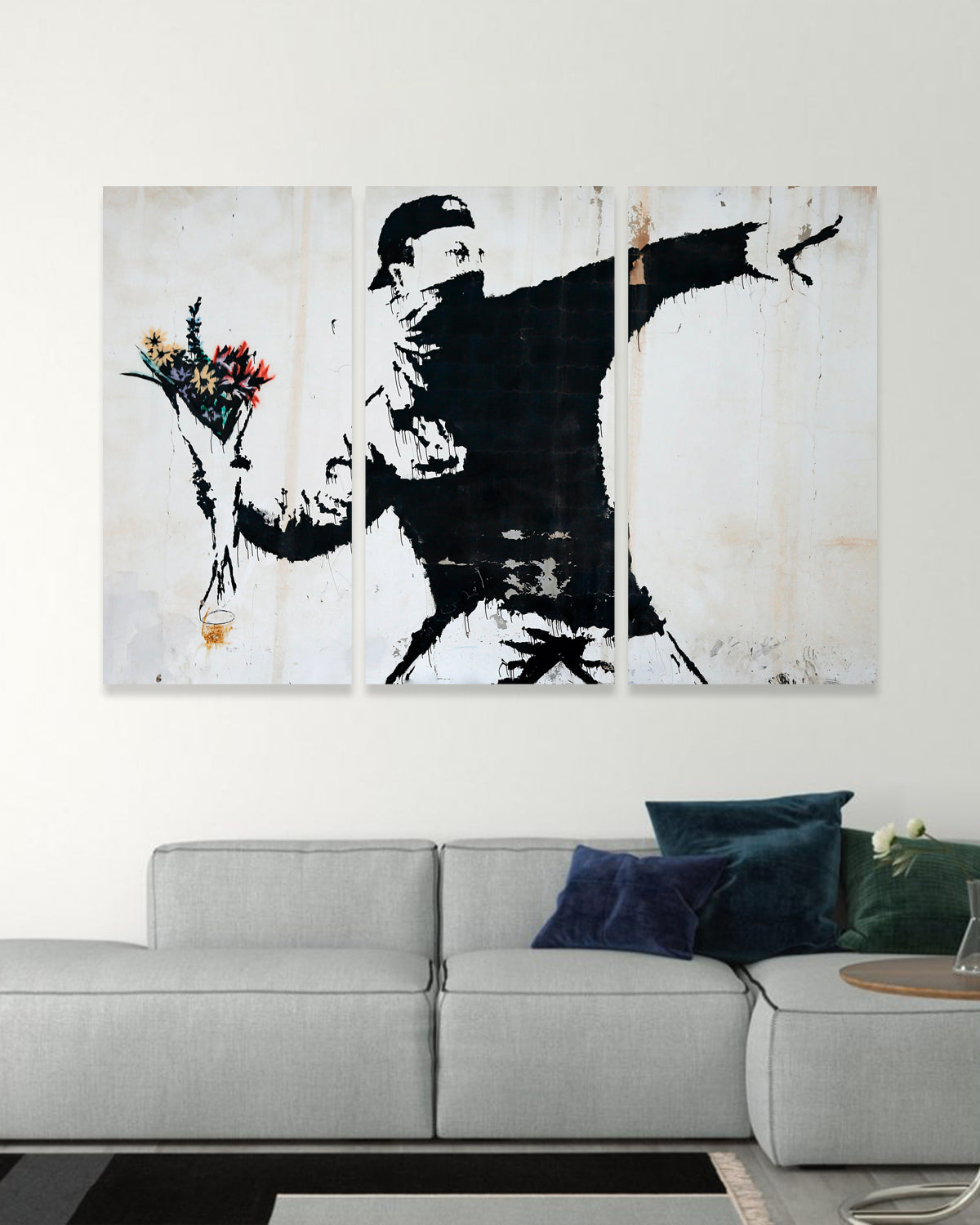 Banksy Flower Grenade - Street art canvas print featuring black silhouette throwing colorful flowers instead of a weapon, symbolic protest artwork displayed above modern grey sofa in contemporary living room setting