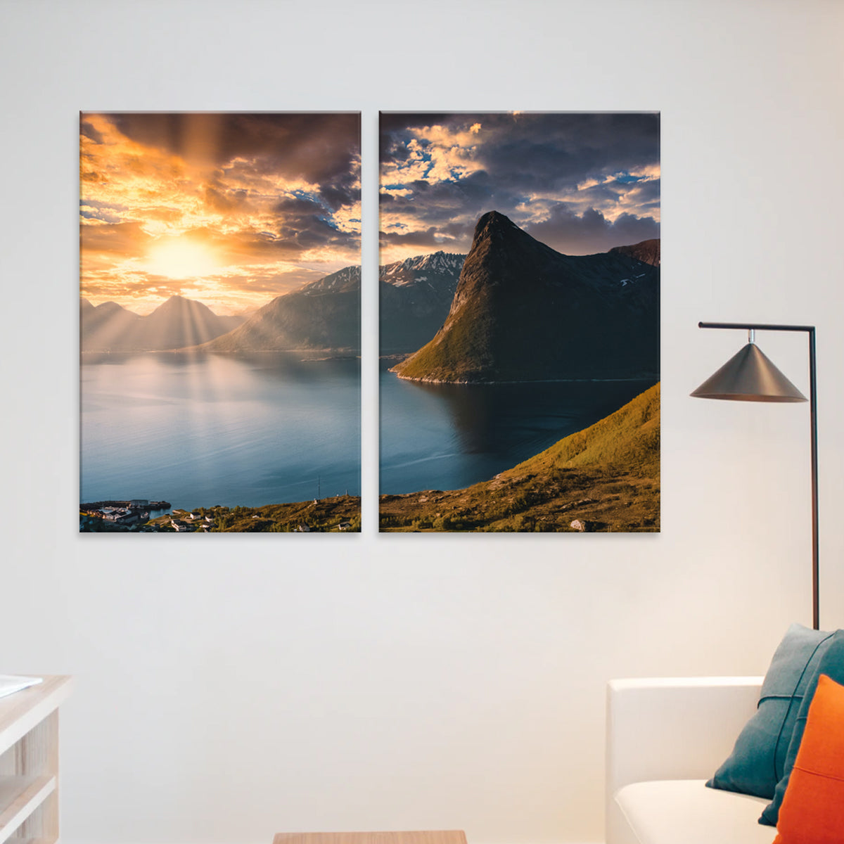 Mountain Sunrise 2-panel canvas print featuring a dramatic fjord landscape at sunset, with sunbeams piercing through golden clouds over calm waters, snow-capped peaks and a prominent rocky peninsula, displayed in a modern living space