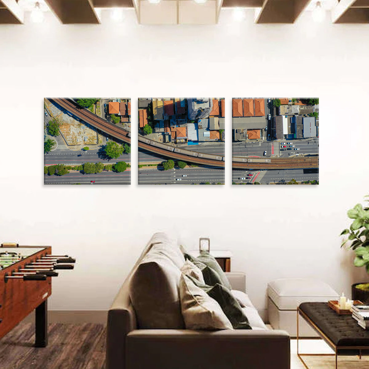 Road and Train: Aerial view triptych canvas art showing urban infrastructure with elevated railway tracks, winding roads, and city buildings in bird's eye perspective, mounted on modern white wall above sofa