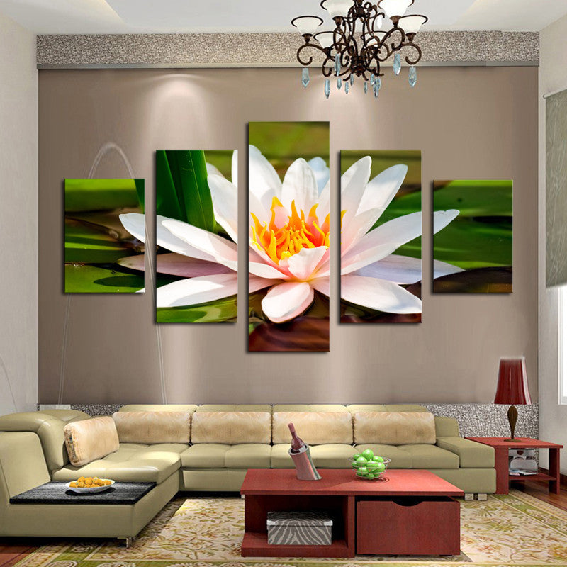 White Flower canvas wall art featuring a beautiful lotus bloom in 5 panels, displaying delicate pink-white petals and yellow center against green leaves, elegantly mounted on beige wall above modern sectional sofa