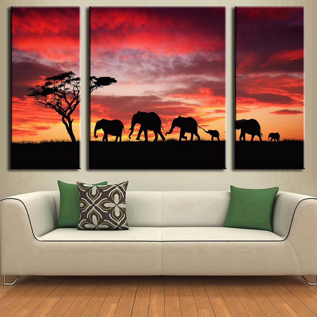 Elephant Safari Red Sky Sunset - Silhouetted family of elephants walking across African savanna against dramatic crimson and orange sunset sky with lone acacia tree, displayed as 3-panel canvas wall art