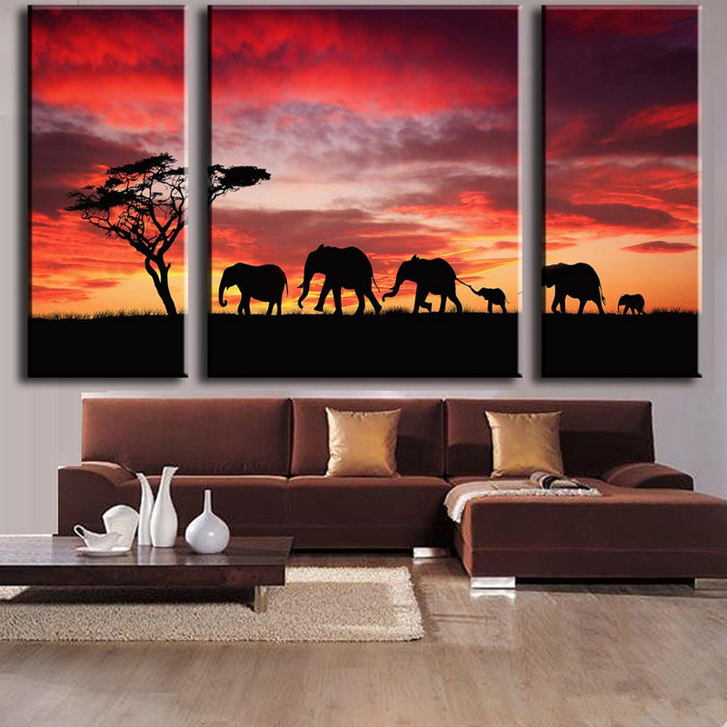 Elephant Safari Red Sky Sunset: Dramatic silhouette of elephant family walking beneath an African acacia tree against vibrant red and orange sunset sky, displayed as three-panel canvas wall art set.