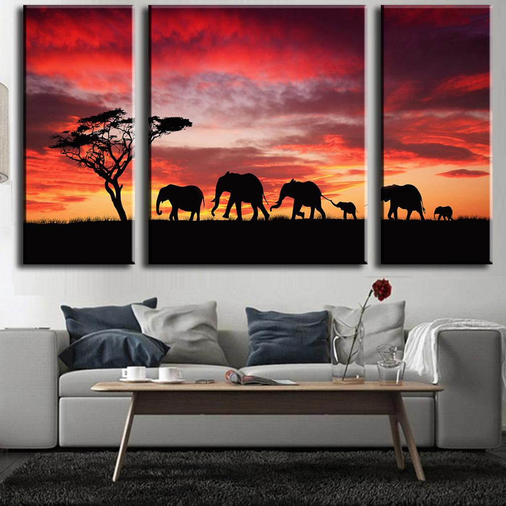 Elephant Safari Red Sky Sunset: Dramatic silhouettes of African elephants walking in line beneath an acacia tree against a vibrant red and orange sunset sky, captured in a stunning 3-panel canvas wall art piece.