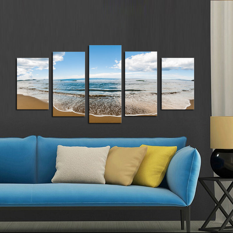 Sprawling Beach - 5-piece canvas wall art featuring serene ocean waves meeting golden sandy shore under bright blue sky with white clouds, displayed above modern blue sofa for coastal home decor