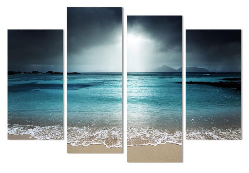 Dark Beach Scene - Moody 4-panel canvas wall art featuring turquoise ocean waters under stormy skies, with gentle waves breaking on sandy shore against distant mountain silhouettes at dusk