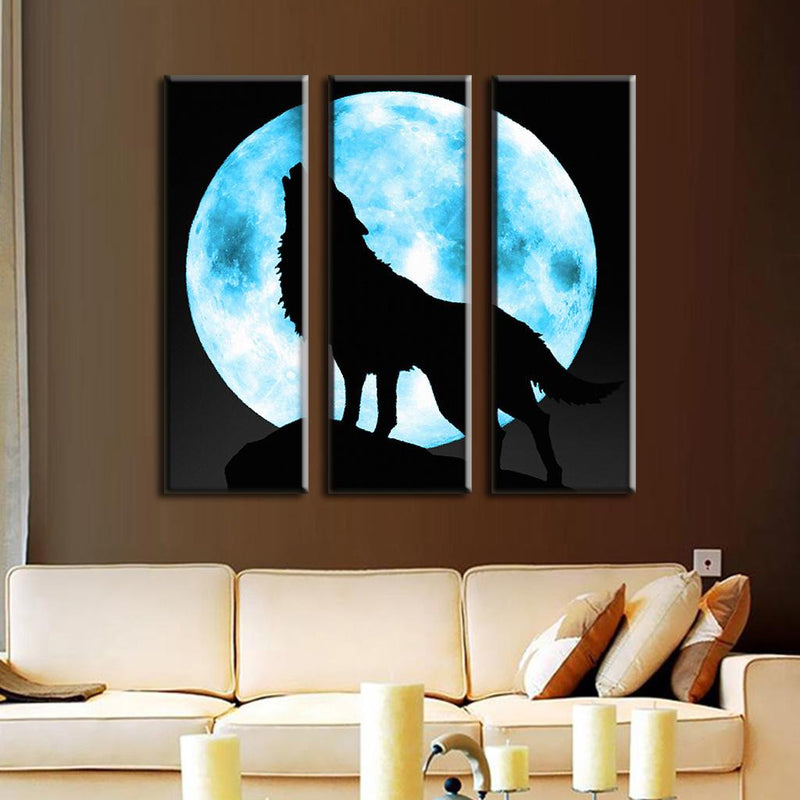 Lone Wolf and Moon - 3-panel canvas wall art featuring silhouette of howling wolf against bright blue full moon, displayed above beige couch in modern living room setting