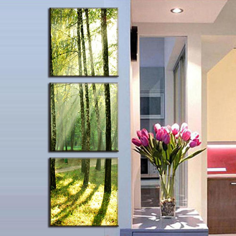 Sunshine Through the Trees: Three-panel canvas wall art displaying sunlight filtering through forest trees creating ethereal green and golden rays, shown in modern home setting with decorative tulips