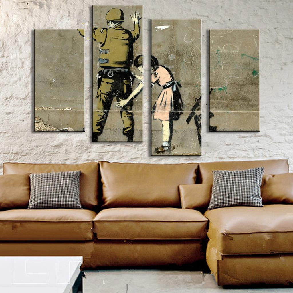 Anti War Banksy Art: 4-panel canvas wall print featuring street art design showing a silhouette of a soldier being searched by a small figure against textured concrete background, displayed above brown leather sectional sofa