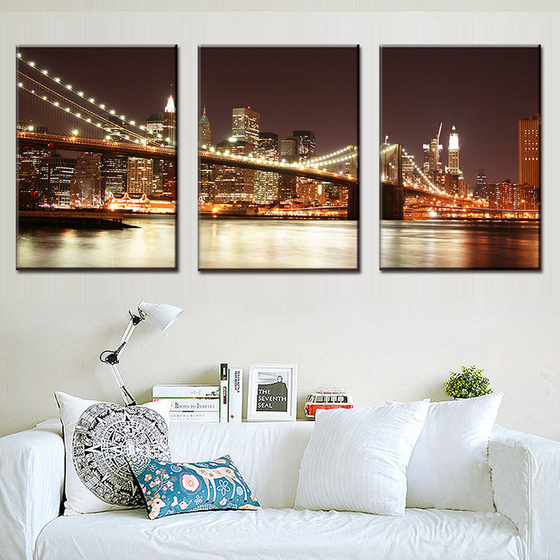 The Brooklyn Bridge at Night 3-piece canvas wall art featuring illuminated bridge spans over East River with glowing Manhattan skyline, city lights reflecting on water, warm sepia tones perfect for modern home decor