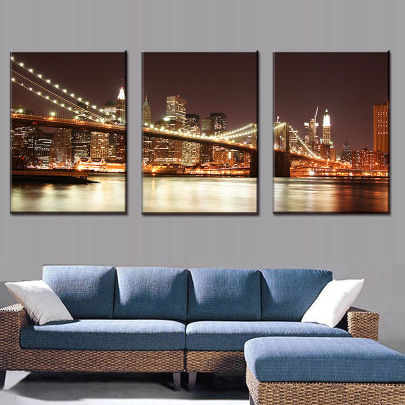 The Brooklyn Bridge at Night - Stunning 3-piece canvas wall art featuring illuminated Brooklyn Bridge spanning East River with Manhattan skyline, glowing city lights reflecting on water at twilight