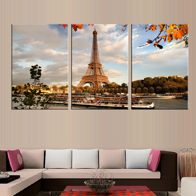 The Eiffel Tower Landscape: Autumn scene of iconic Paris tower against sunset sky, with Seine River boats below and orange fall leaves framing scenic three-panel canvas wall art