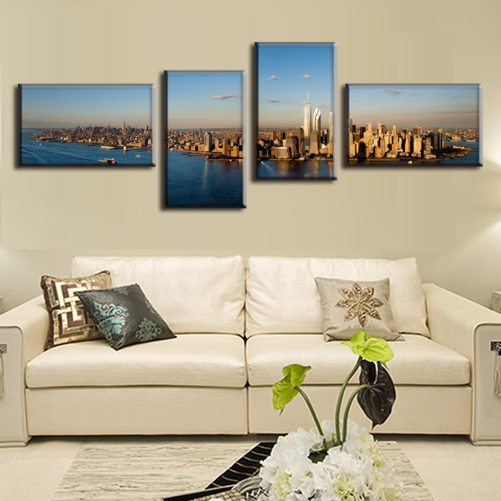 New York City Panorama: 4-panel canvas wall art displaying aerial view of Manhattan skyline, Hudson River, and iconic skyscrapers bathed in golden sunlight against blue sky, mounted above cream-colored sofa