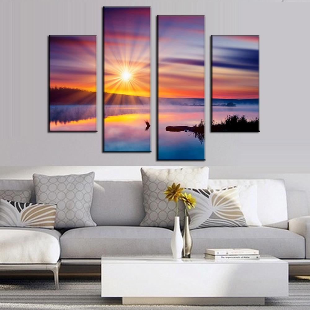 Colorful Sunset with Glare - 4-panel canvas wall art featuring vibrant sunset over tranquil lake, bright sunburst reflecting on calm water with silhouetted driftwood and shoreline, displayed in modern living room setting