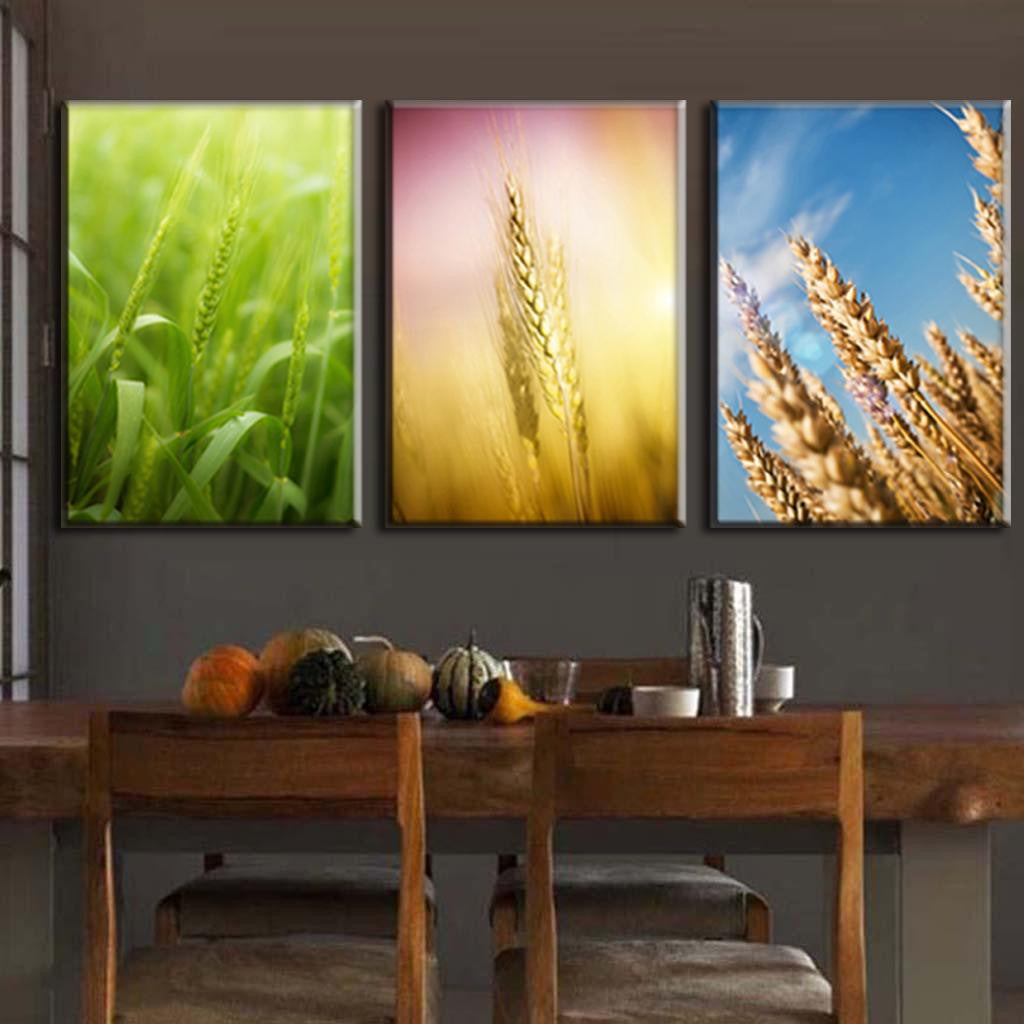 Modern Wheat Set: Three-panel canvas wall art featuring vibrant wheat stalks in different stages, from fresh green growth to golden mature wheat, displayed against varied sky backgrounds above wooden dining furniture
