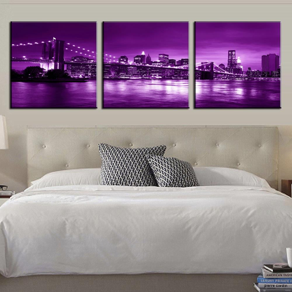 Brooklyn Bridge in Purple Night - 3-panel canvas wall art displaying New York City skyline with illuminated bridge and skyscrapers reflected in water under vibrant purple twilight sky