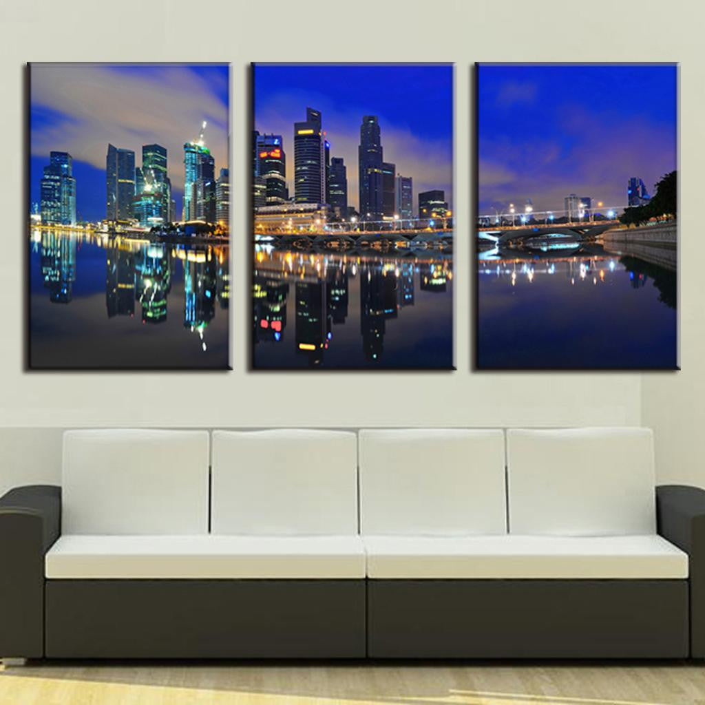 Modern City at Night - 3-panel canvas art featuring illuminated skyscrapers reflecting in calm water at twilight, with vibrant blue sky and city lights creating a stunning mirror effect across the harbor