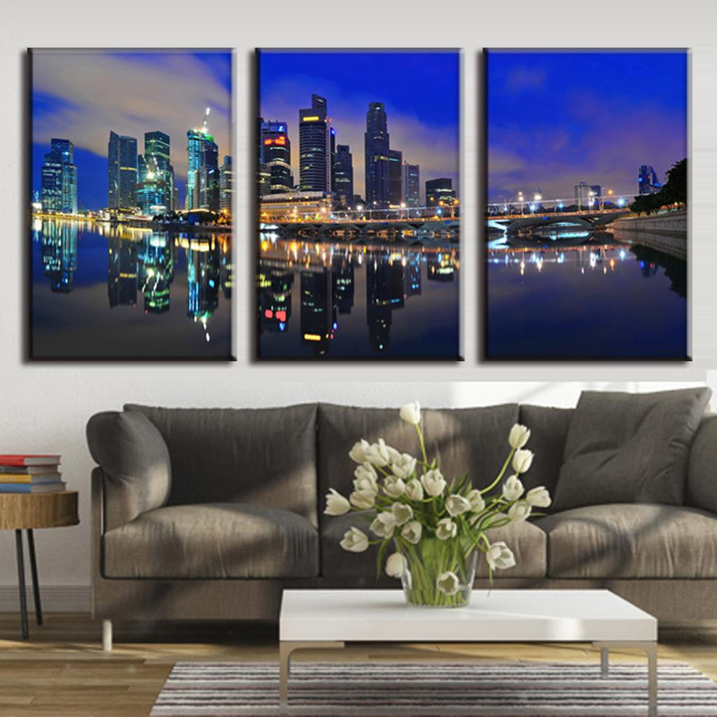 Modern City at Night - spectacular illuminated cityscape with gleaming skyscrapers reflecting in calm waterfront, 3-panel canvas wall art featuring dramatic blue twilight sky and mirror-like water reflections