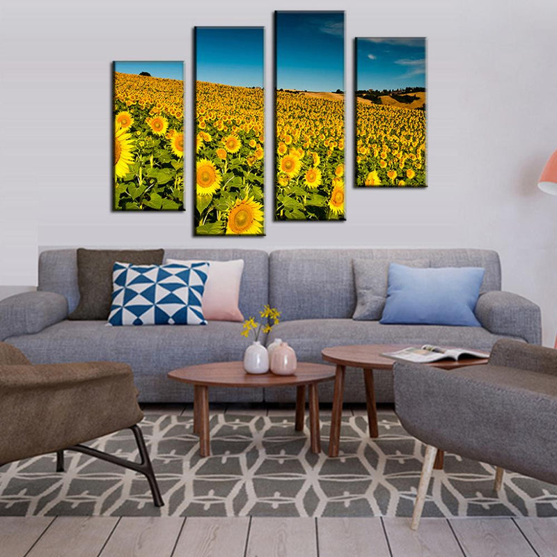 Field of Sunflowers wall art showing vibrant yellow sunflower field stretching to horizon under bright blue sky, displayed as 4-panel canvas print above modern grey sectional sofa in contemporary living room setting