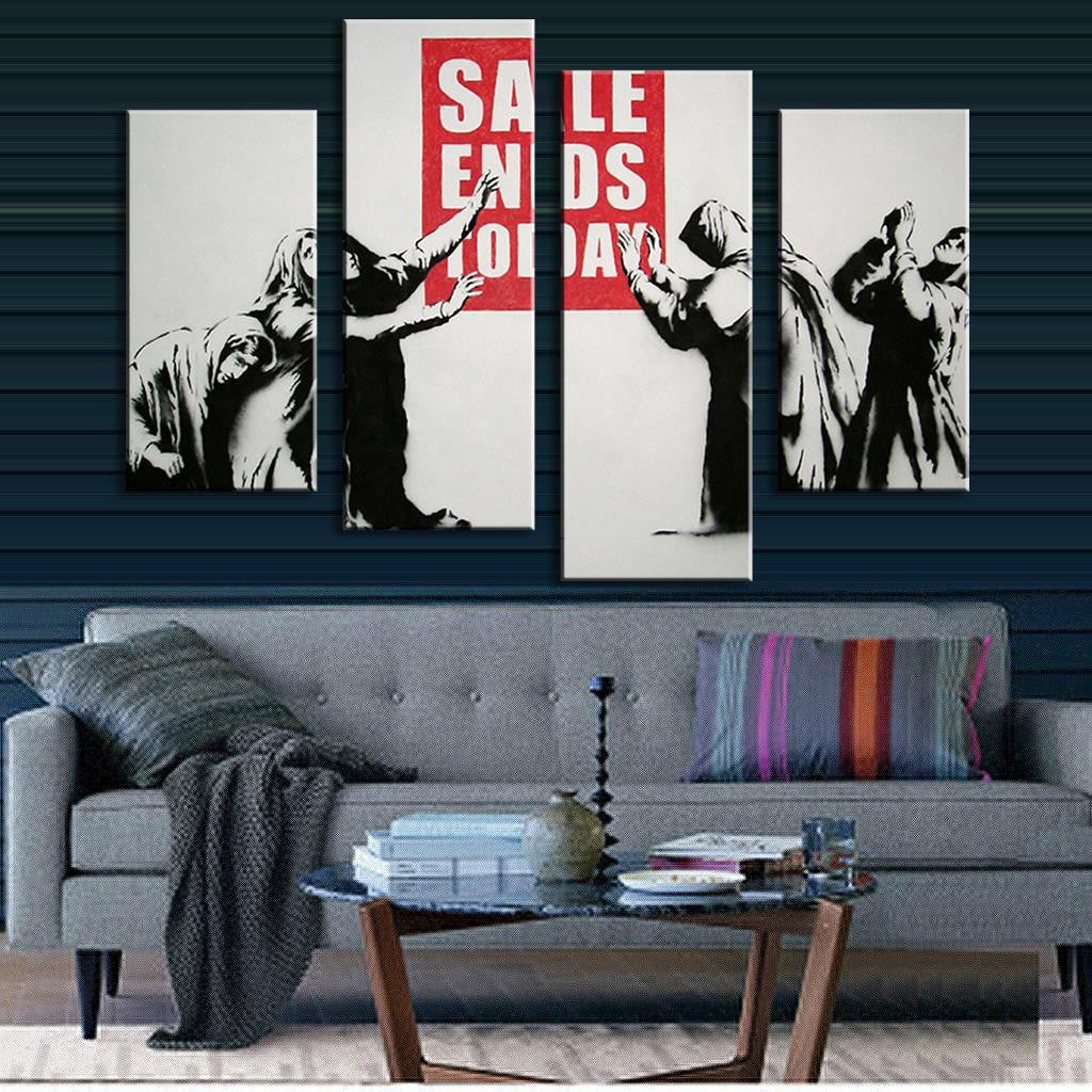 Banksy Sale Ends Today: 4-piece canvas wall art depicting figures in black and white reaching for a red sale sign, displayed above a modern grey sofa in a contemporary living room setting