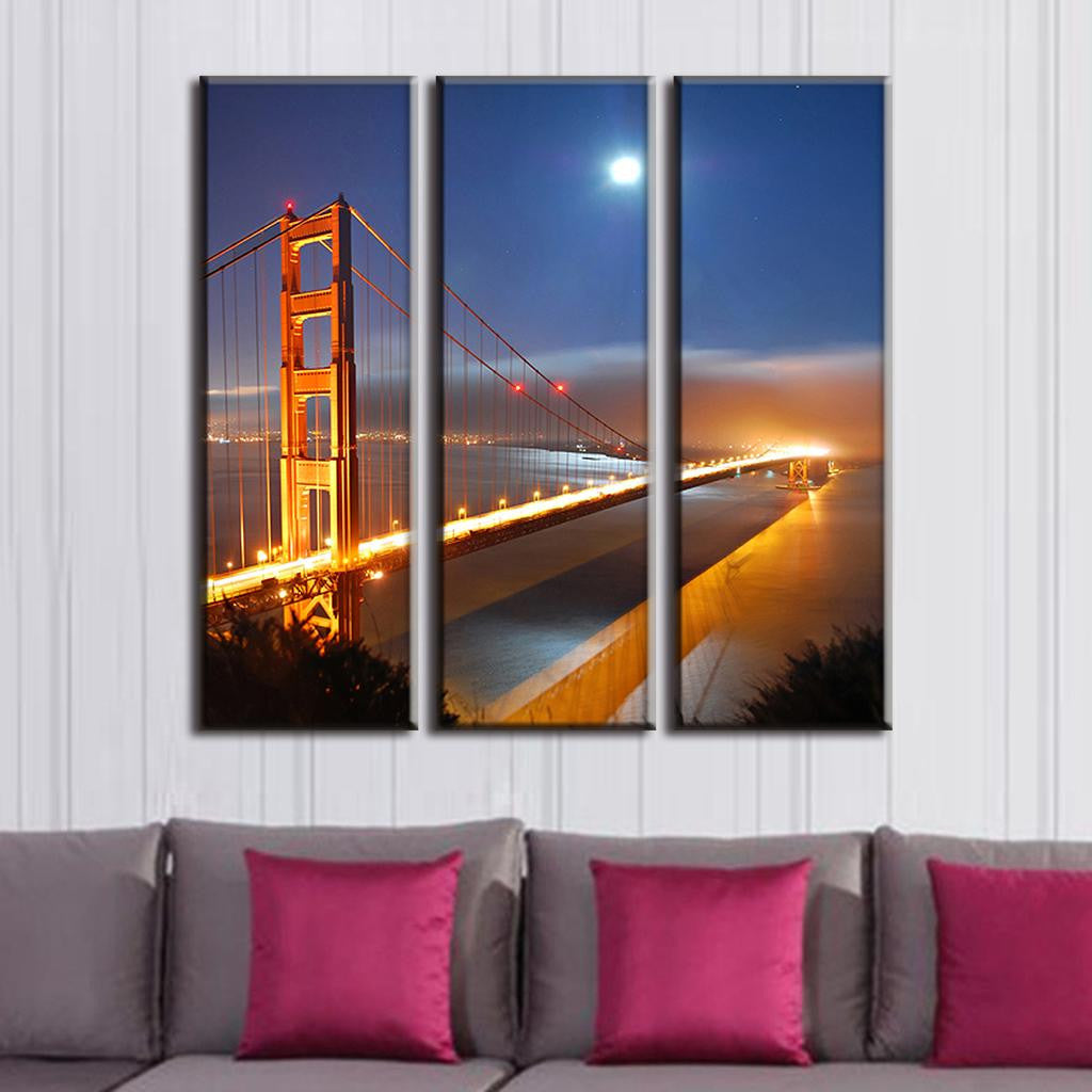 Golden Gate Bridge Under Moonlight - Three-panel canvas art showing iconic San Francisco bridge illuminated at night with bright full moon, glowing bridge lights reflecting on water, vibrant orange towers against deep blue sky