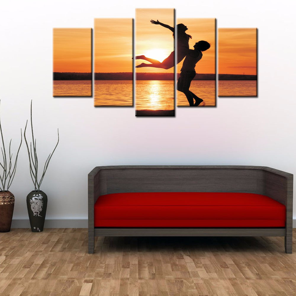 Uplifted Silhouettes - 5-panel canvas wall art featuring silhouettes of two people leaping joyfully against a vibrant orange sunset over calm water, creating a dramatic and inspiring beach scene