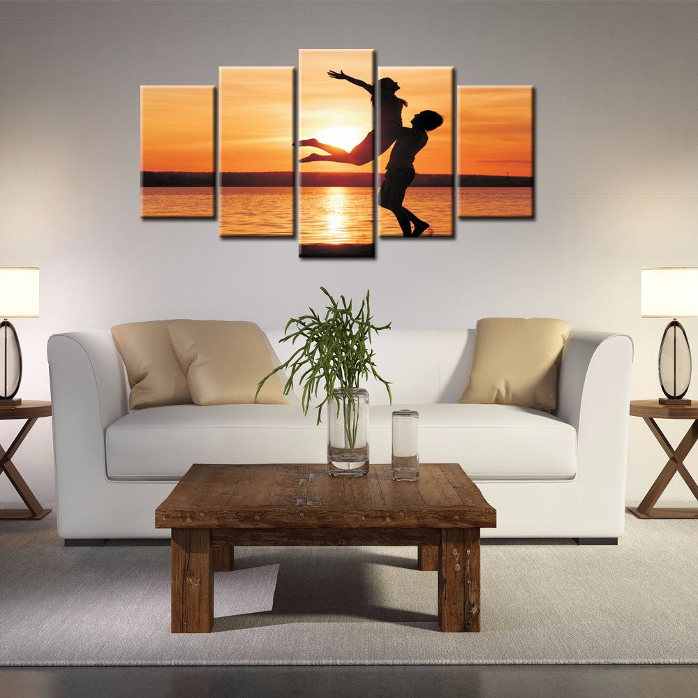 Uplifted Silhouettes: 5-panel canvas wall art featuring silhouetted figures leaping joyfully against a vibrant orange sunset over calm water, creating a dramatic and inspiring scene for modern home decor