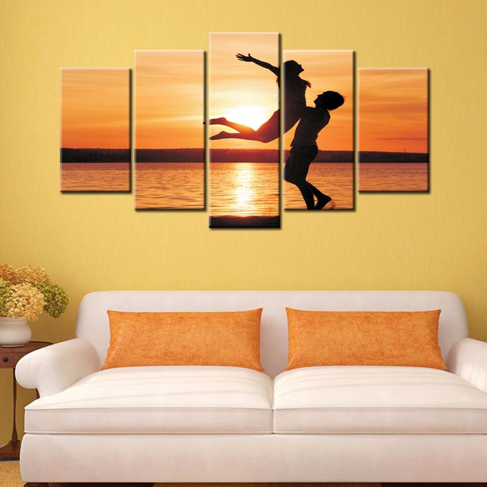Uplifted Silhouettes 5-panel canvas wall art featuring silhouetted figures against vibrant orange sunset over water, creating romantic and joyful scene with warm tones perfect for home decor