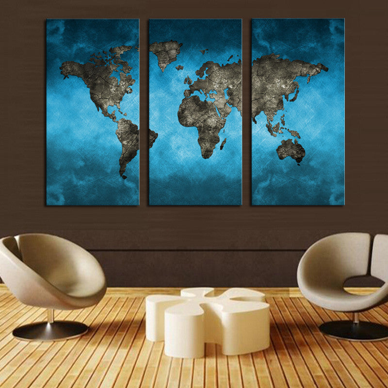 Blue World Map Art: Modern 3-panel canvas wall art featuring a detailed world map in striking metallic gray against a vibrant turquoise blue background, displayed in a contemporary living room setting