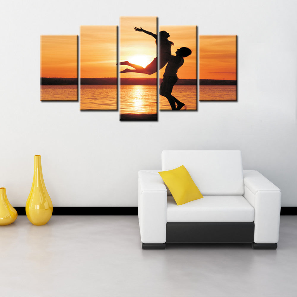 Uplifted Silhouettes: Five-panel canvas art featuring two silhouettes dancing against a vibrant orange sunset over water, creating a romantic and dynamic scene with golden reflections on the water's surface